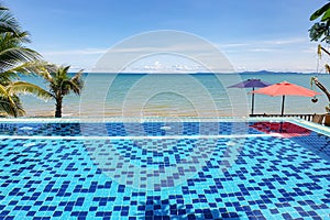 Mosaic swimming pool in sea front hotel resort with ocean sea sand beach and blue sky background landscape