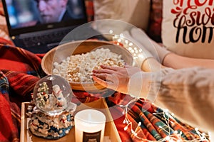 Moscow 11.29.2021. female hand eat popcorn food and enjoyment relaxing watching the movie `home alone` on laptop at home in comf