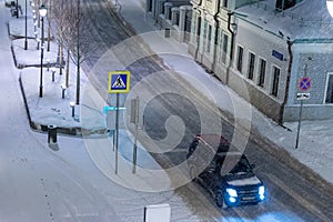 Moscow, Russia - December 27, 2022: Car drives down a snowy street in a cold and deserted Moscow on a dark winter evening