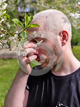 A man rubbing his nose suffering from the seasonal pollen allergy attack standing next to the flowering tree in the spring park.