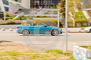 Blue convertible car BMW F33 4-series at the city street in motion. Side view of fast moving BMW cabrio