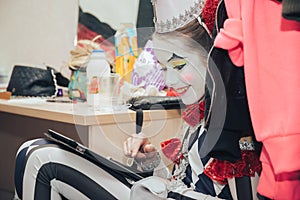 Girl clown in makeup sitting in the dressing room resting.