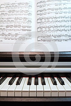 An open book of sheet music on the piano. A composition of the sheet music and the piano keyboard.