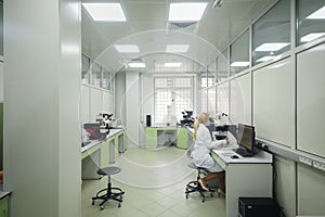 Woman looks through microscope in lab of Forensic photo