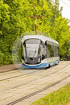 Moscow tram goes on rails against foliage. Modern urban rail electric ecological transport, vertical photo