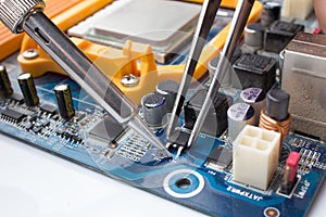 A MOSFET transistor key is soldered out of computer Board using a soldering iron and tweezers photo