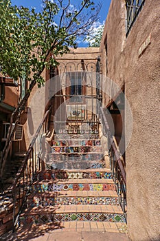 Mosiac steps leading up to second story entrance and a locked iron gate in an adobe building