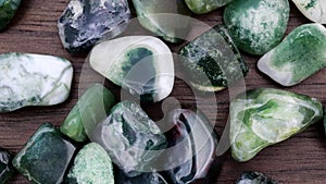 Moss agate heap up jewel stones texture on brown varnished wood background. Moving right seamless loop backdrop