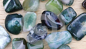 Moss agate heap up jewel stones texture on light varnished wood background. Moving right seamless loop backdrop