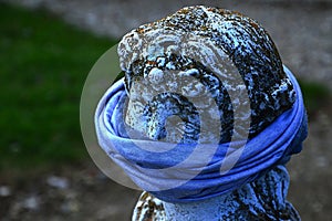 Moss covered stone statue head in ancient Greek or Roman style with bandana scarf on her mouth as a face mask.