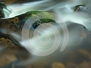 Mossy stone in blurred blue waves of mountain stream. Cold water is running and turning between boulders and bubbles create tr