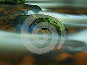 Mossy stone with grass in the mountain stream. Fresh colors of grass, deep green color of wet moss and blue milky water