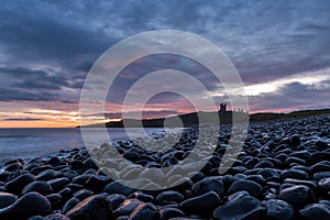 The most beautiful sunrise at Dunstanburgh Castle with the famous slippery black boulders in Northumberland, as the sky erupted wi