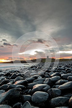 The most beautiful sunrise at Dunstanburgh Castle with the famous slippery black boulders in Northumberland, as the sky erupted wi