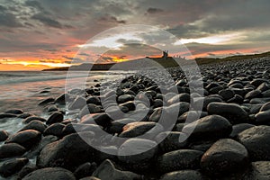 The most beautiful sunrise at Dunstanburgh Castle with the famous slippery black boulders in Northumberland, as the sky erupted wi