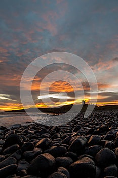 The most beautiful sunrise at Dunstanburgh Castle with the famous slippery black boulders in Northumberland, as the sky erupted wi