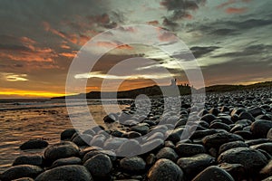 The most beautiful sunrise at Dunstanburgh Castle with the famous slippery black boulders in Northumberland, as the sky erupted wi