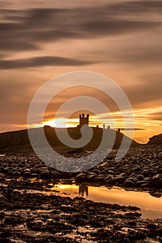 The most beautiful sunrise at Dunstanburgh Castle with the famous slippery black boulders in Northumberland, as the sky erupted wi