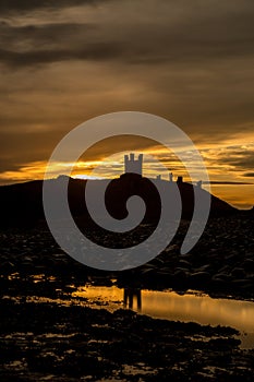 The most beautiful sunrise at Dunstanburgh Castle with the famous slippery black boulders in Northumberland, as the sky erupted wi