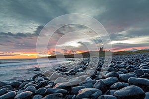 The most beautiful sunrise at Dunstanburgh Castle with the famous slippery black boulders in Northumberland, as the sky erupted wi