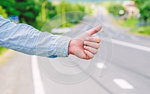 Most popular way of hitchhiking is to thumb up. Hand thumb up gesture try stop car road background. Thumb or hand