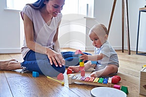 Mother With 8 Month Old Baby Son Learning Through Playing With Coloured Wooden Blocks At Home