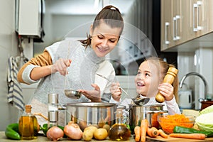 Mother add pepper to vegetable soup and small daughter tasting