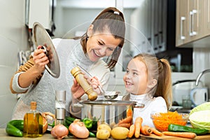 Mother add pepper to vegetable soup and small daughter tasting