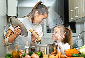 Mother add pepper to vegetable soup and small daughter tasting