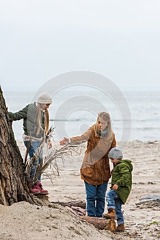 mother and adorable little kids spending time together on seashore on cold
