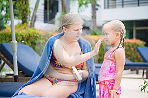 Mother applies suntan lotion to daughter face near pool in tropical beach resort