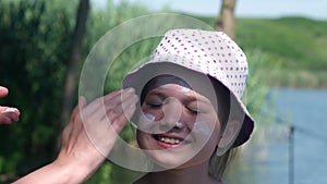 Mother apply protective sunscreen on daughter face at riverbank in summertime