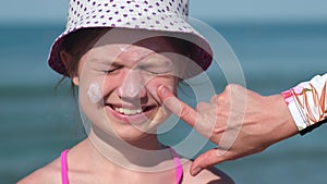 Mother apply protective sunscreen on daughter nose at beach on summer vacation