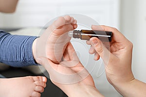 Mother applying essential oil from roller bottle onto her baby`s heel on blurred background, closeup