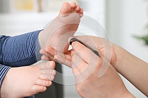 Mother applying essential oil from roller bottle onto her baby`s heel on blurred background, closeup