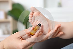 Mother applying essential oil from roller bottle onto her baby`s heel indoors, closeup