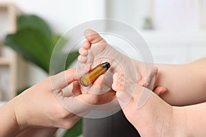 Mother applying essential oil from roller bottle onto her baby`s heel indoors, closeup