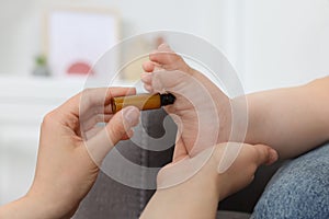 Mother applying essential oil from roller bottle onto her baby`s heel indoors, closeup