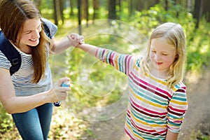 Mother applying insect repellent to her daughter before forest hike summer day. Protecting children from biting insects at summer
