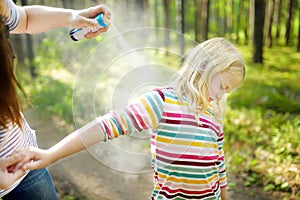 Mother applying insect repellent to her daughter before forest hike summer day. Protecting children from biting insects at summer