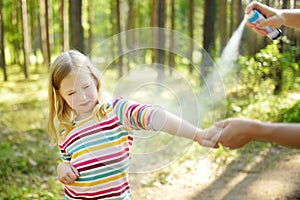 Mother applying insect repellent to her daughter before forest hike summer day. Protecting children from biting insects at summer