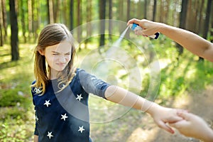 Mother applying insect repellent to her daughter before forest hike summer day. Protecting children from biting insects at summer