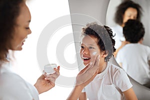 Mother Applying Moisturizer on Sons Face in Bright Bathroom