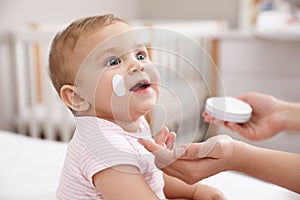 Mother applying moisturizing cream on her little baby at home, closeup