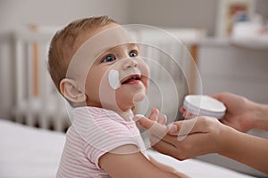 Mother applying moisturizing cream on her little baby at home, closeup