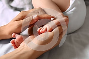 Mother applying moisturizing cream onto baby`s foot on bed, closeup