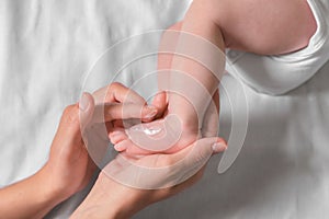 Mother applying moisturizing cream onto baby`s foot on bed, top view