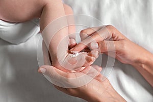 Mother applying moisturizing cream onto baby`s foot on bed, top view