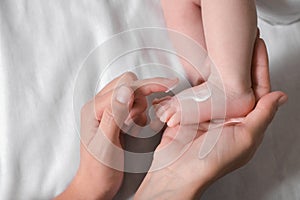 Mother applying moisturizing cream onto baby`s foot on bed, top view