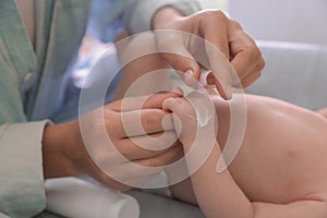 Mother applying moisturizing cream onto baby`s hand on changing table, closeup